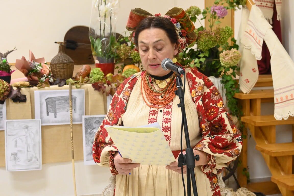 A member in folk costume reading at a cultural presentation